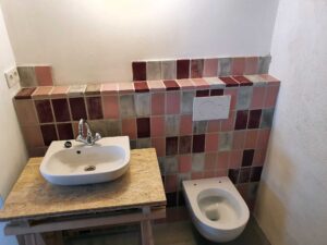 Bathroom with multicolored square tile wall and counter-mounted sink; a wall-mounted dual-flush toilet is visible on the right side.