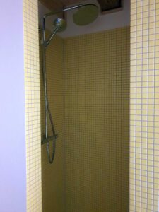 Shower area with yellow tiled walls and chrome shower fixtures, including a ceiling-mounted rain shower and a handheld wand.