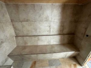 Built-in tiled shower bench with two levels in a gray-tiled bathroom area.
