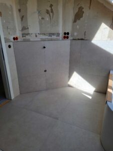 Under-construction bathroom with gray tiled walls and floor; red-capped pipe openings along the right edge.