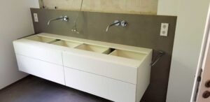 White bathroom vanity with two open drawers, gray backsplash, and exposed plumbing—under construction?cleanup ongoing.