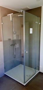 Glass-walled shower enclosure with chrome hardware, a handheld shower head on a vertical rail, and grey tile walls inside.
