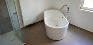 Minimalist bathroom with a white freestanding bathtub and chrome floor-mounted faucet, beside a glass-enclosed shower and a window letting in light.
