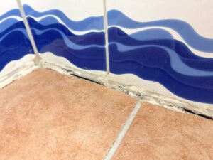 Corner of blue wave-pattern ceramic tiles meeting brown floor tiles; noticeable grout cracks at the corner.