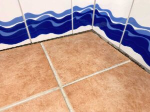Corner of a room showing brown square floor tiles meeting a wall with blue wavy stripe mural at the corner.