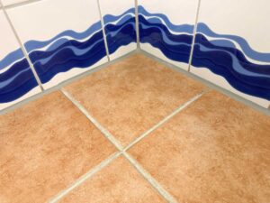 Corner of a tiled wall with a blue wavy stripe design meeting brown floor tiles at a corner.
