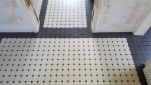 Tile floor in a doorway hallway with white square tiles that have small black centers, bordered by dark gray tiles on the edges.