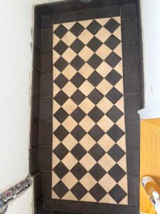 Checkerboard tile floor with beige and black diamonds, bordered by a dark tile frame in a doorway area.